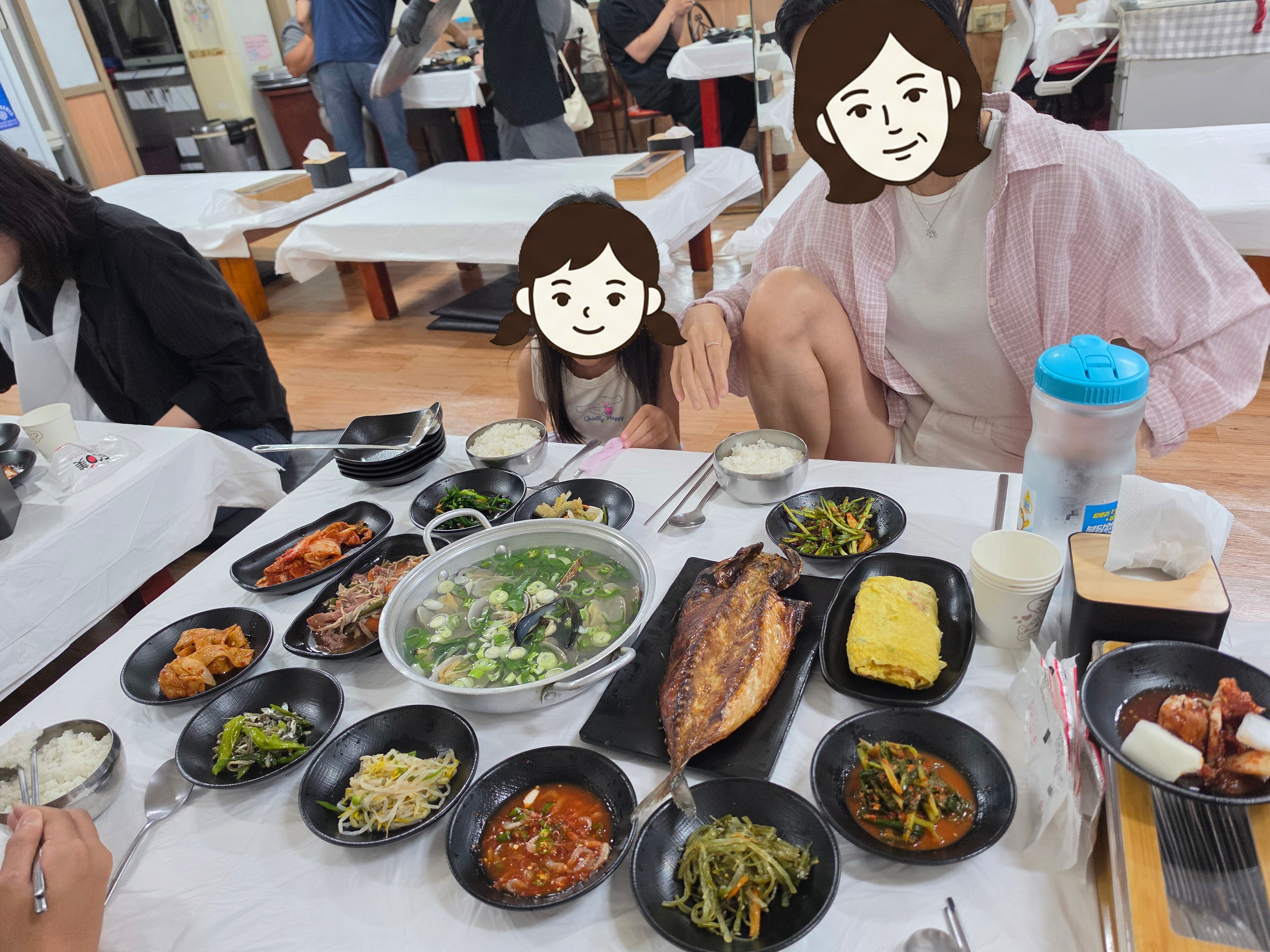 백성식당 상 위에 가득 차려진 반찬들과 조개탕, 생선구이, 그리고 식사 중인 엄마와 모아